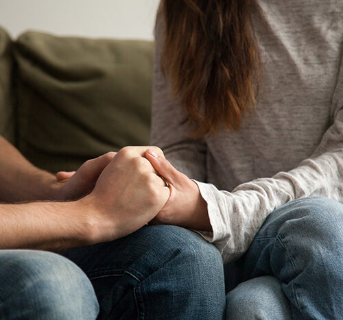 Two people clasp hands and talk, taking an important step in healing relationships in recovery.